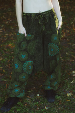 Kobieta w czarnym topie i zielonych szarawarach ze wzorem mandali stoi na tle zieleni