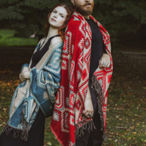 Kobieta i mężczyzna stoją oparci o siebie w parku ubrani w czarne ubrania i kolorowe szale w etno wzory