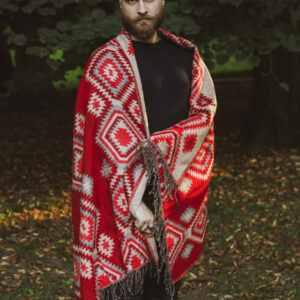 Meżczyzna ubrany na czarno stoi w parku owinięty w czerwony etno szal