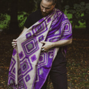 Meżczyzna ubrany na czarno stoi w parku owinięty w fioletowy etno szal