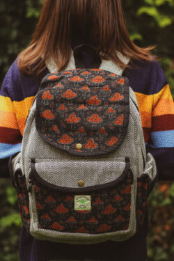 Kobieta w sweterku w paski ma stoi tyłem z dużym plecakiem w kolorze czarnym z nadrukami muchomorków