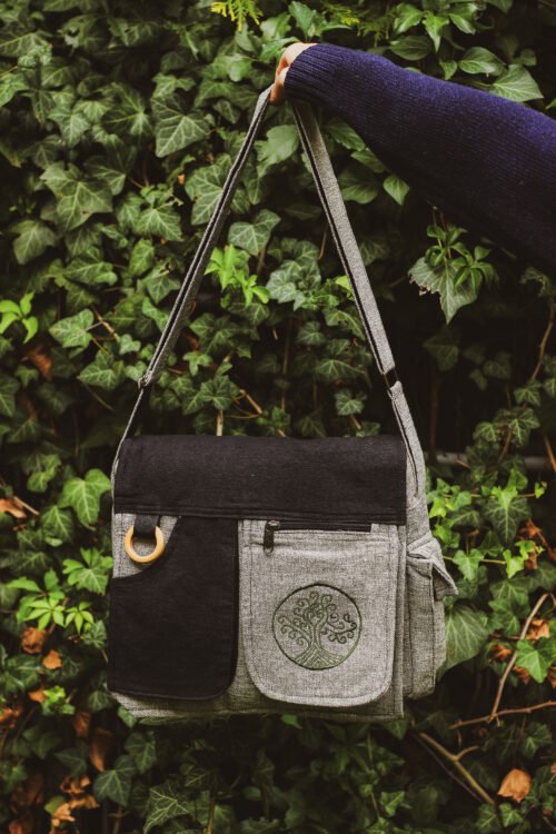 Osoba trzyma szaro-czarną torebkę A4 z zielonym haftem Drzewa Życia na tle zieleni