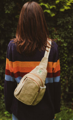 Kobieta w swetrze w paski z trójkątnym, beżowym plecakiem Himalayan Hemp stoi na tle zieleni