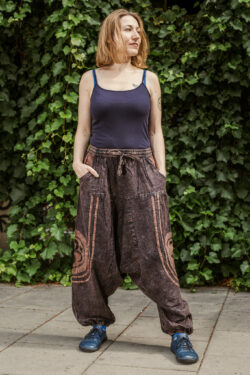 Kobieta z blond włosami ubrana w czarny podkoszulek i brązowe szarawary stoi na tle bluszczu