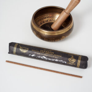 Kadzidło tybetańskie Ultabati w czarnym opakowaniu leży na białym tle obok złotej misy dźwiękowej