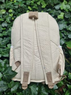 Tylna beżowa część plecaka z kieszeniami po bokach leżącego na bluszczu