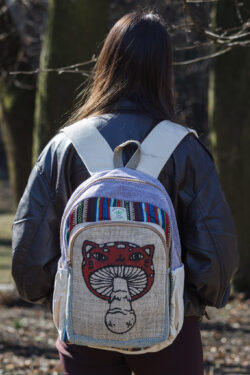 Osoba w czarnej skórzanej kurtce stoi tyłem w parku i ma na plecach beżowo fioletowo czerwony plecak z ilustracją muchomora z podobizną kota wykonany z beżowej konopi i kolorowego materiału gheri