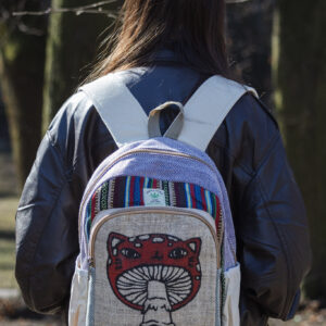 Osoba w czarnej skórzanej kurtce stoi tyłem w parku i ma na plecach beżowo fioletowo czerwony plecak z ilustracją muchomora z podobizną kota wykonany z beżowej konopi i kolorowego materiału gheri