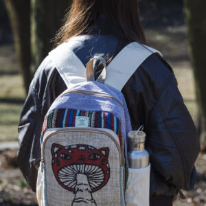 Osoba w czarnej skórzanej kurtce stoi tyłem w parku i ma na plecach beżowo fioletowo czerwony plecak z ilustracją muchomora z podobizną kota wykonany z beżowej konopi i kolorowego materiału gheri w bocznej kieszeni znajduje się srebrny bidon