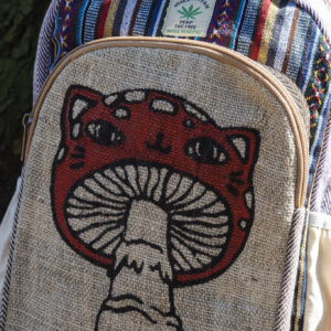 Kolorowy plecak leży na ziemi przy drzewie, ma beżowe kieszenie po bokach, jest wielkości A4 i wykonany z bawełny gheri oraz konopi, na przedniej kieszeni znajduje się ilustracja muchomora o podobiźnie kota