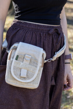 Osoba nosząca beżową torebkę z konopi i bawełny na mały aparat, z odpinanym paskiem, klapą i zamkami, na tle trawy