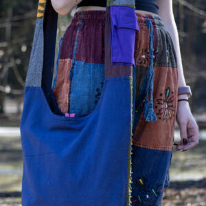 Osoba w kolorowych spodniach i czarnym topie prezentuje tył torby na ramieniu w niebieskim kolorze z fioletową kieszonką na pasku