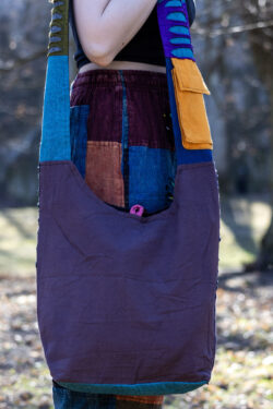 Osoba w kolorowych spodniach i czarnym topie prezentuje tył torby na ramieniu w niebieskim kolorze z fioletową kieszonką na pasku