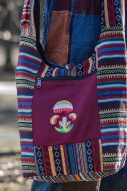 Osoba w kolorowych spodniach ma na ramieniu torbę z materiału gheri i ilustracją pomarańczowych grzybów na tle trawy