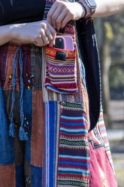 Osoba w kolorowych spodniach wkłada telefon do kieszeni torby patchworkowej na ramieniu