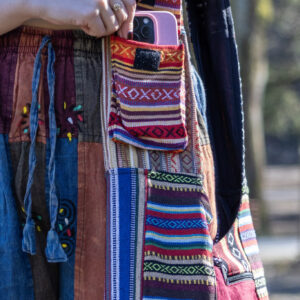 Osoba w kolorowych spodniach wkłada telefon do kieszeni torby patchworkowej na ramieniu