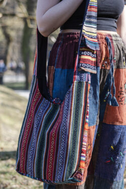 Osoba w kolorowych spodniach ma na ramieniu patchworkową torbę z materiałem gheri w parku