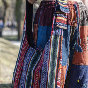 Osoba w kolorowych spodniach ma na ramieniu patchworkową torbę z materiałem gheri w parku