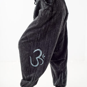 Kobieta stoi bokiem na białym tle i ma na sobie czarny top oraz luźne szare bawełniane szarawary we wzór om