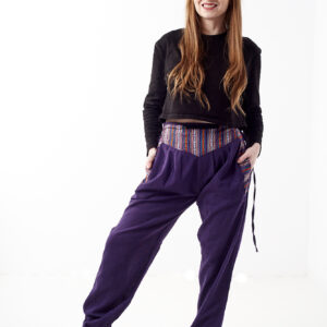 Osoba w czarnej koszulce stoi na białym tle w fioletowych spodniach z wstawkami z materiału gheri