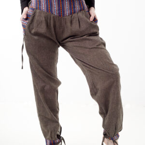 Kobieta na białym tle w czarnym topie i brązowych, luźnych bawełnianych spodniach z wiązaniami na nogawkach oraz wykończeniami we wzór gheri, z przodu znajduje się rozpinana kieszeń