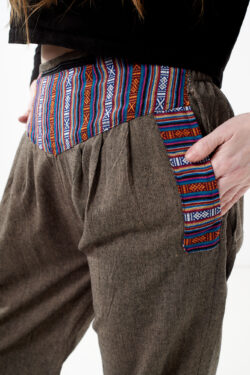 Osoba na białym tle w czarnym topie i brązowych, luźnych bawełnianych spodniach z wiązaniami na nogawkach oraz wykończeniami we wzór gheri, z przodu znajduje się rozpinana kieszeń