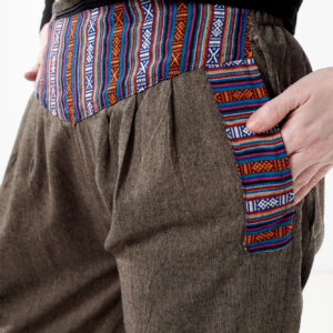 Osoba na białym tle w czarnym topie i brązowych, luźnych bawełnianych spodniach z wiązaniami na nogawkach oraz wykończeniami we wzór gheri, z przodu znajduje się rozpinana kieszeń