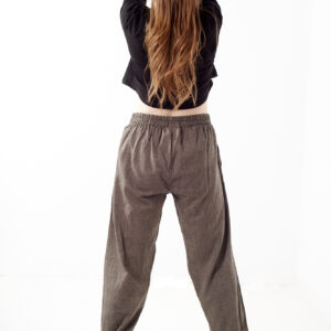 Kobieta na białym tle stoi tyłem w czarnym topie i brązowych, luźnych bawełnianych spodniach z wiązaniami na nogawkach oraz wykończeniami we wzór gheri