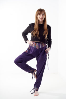 Osoba w czarnej koszulce stoi na białym tle w fioletowych spodniach z wstawkami z materiału gheri