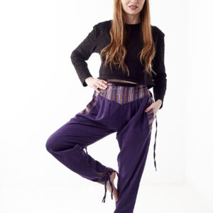 Osoba w czarnej koszulce stoi na białym tle w fioletowych spodniach z wstawkami z materiału gheri