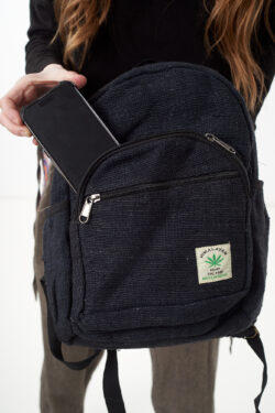 Osoba wkłada telefon do przedniej kieszeni czarnego plecaka z konopi, kieszeń jest zapinana na rzep