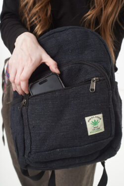 Osoba wkłada telefon do przedniej kieszeni czarnego plecaka z konopi, kieszeń jest zapinana na rzep