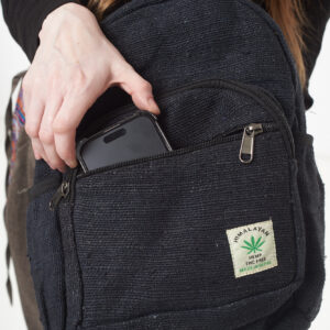 Osoba wkłada telefon do przedniej kieszeni czarnego plecaka z konopi, kieszeń jest zapinana na rzep
