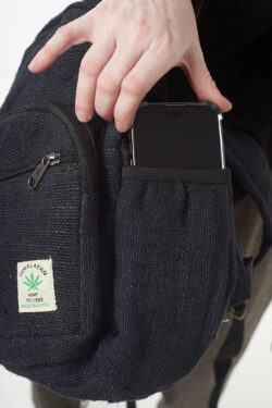 Osoba na białym tle wkłada telefon do bocznej kieszeni czarnego plecaka z konopi, kieszeń jest zapinana na rzep
