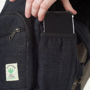 Osoba na białym tle wkłada telefon do bocznej kieszeni czarnego plecaka z konopi, kieszeń jest zapinana na rzep