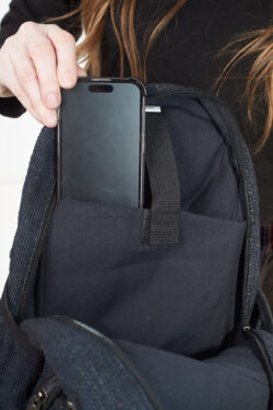 Osoba wkłada telefon do wewnętrznej kieszeni czarnego plecaka z konopi, kieszeń jest zapinana na rzep