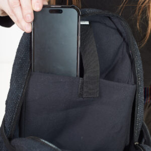 Osoba wkłada telefon do wewnętrznej kieszeni czarnego plecaka z konopi, kieszeń jest zapinana na rzep