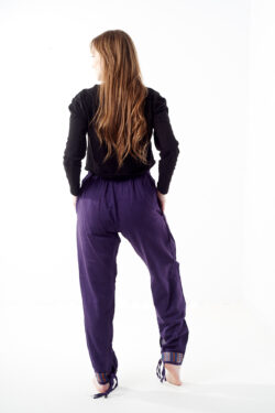 Osoba w czarnej koszulce stoi tyłem na białym tle w fioletowych spodniach z wstawkami z materiału gheri