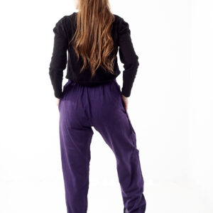 Osoba w czarnej koszulce stoi tyłem na białym tle w fioletowych spodniach z wstawkami z materiału gheri