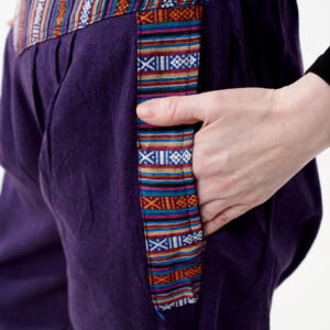 Osoba w czarnej koszulce wkłada rękę do kieszeni fioletowych spodni z wstawkami gheri na białym tle