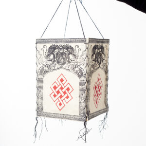 Ręka trzyma beżowy lampion z czerpanego papieru z ilustracją czerwonego węzła nieskończoności i czarnych smoków, na białym tle