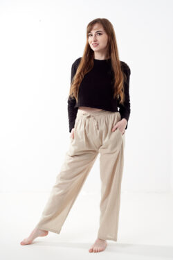 Kobieta w czarnej koszulce wkłada rękę do kieszeni luźnych beżowych spodni na białym tle