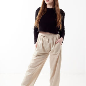 Kobieta w czarnej koszulce wkłada rękę do kieszeni luźnych beżowych spodni na białym tle