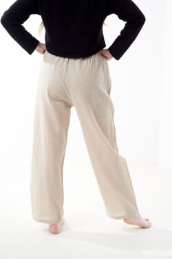 Osoba stoi tyłem na białym tle w czarnej koszulce i luźnych beżowych spodniach