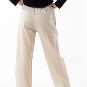 Osoba stoi tyłem na białym tle w czarnej koszulce i luźnych beżowych spodniach