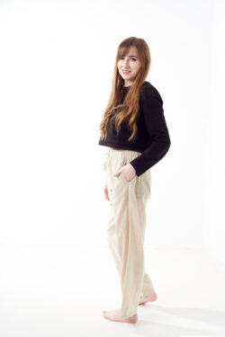 Kobieta w czarnej koszulce wkłada rękę do kieszeni luźnych beżowych spodni na białym tle