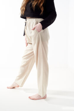 Osoba w czarnej koszulce wkłada rękę do kieszeni luźnych beżowych spodni na białym tle