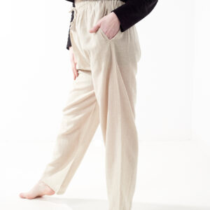 Osoba w czarnej koszulce wkłada rękę do kieszeni luźnych beżowych spodni na białym tle