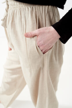 Osoba w czarnej koszulce wkłada rękę do kieszeni luźnych beżowych spodni na białym tle