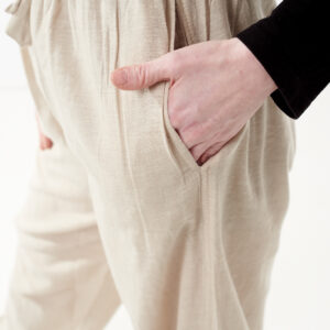 Osoba w czarnej koszulce wkłada rękę do kieszeni luźnych beżowych spodni na białym tle